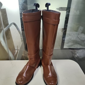 May include: A pair of brown leather knee-high boots with a buckle detail on the shaft.