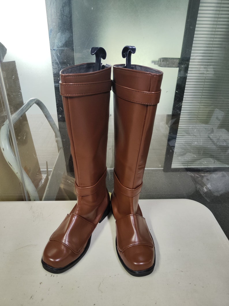 May include: A pair of brown leather knee-high boots with a buckle detail on the shaft.