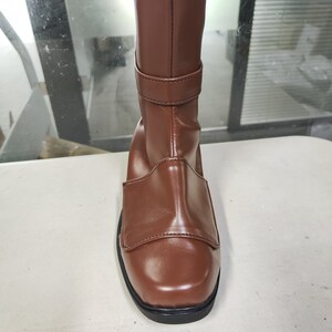 May include: Brown leather knee-high boots with a buckle strap and a square toe.