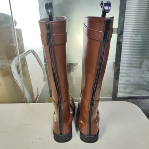 May include: A pair of brown leather knee-high boots with black zips on the back. The boots have a buckle detail on the side.