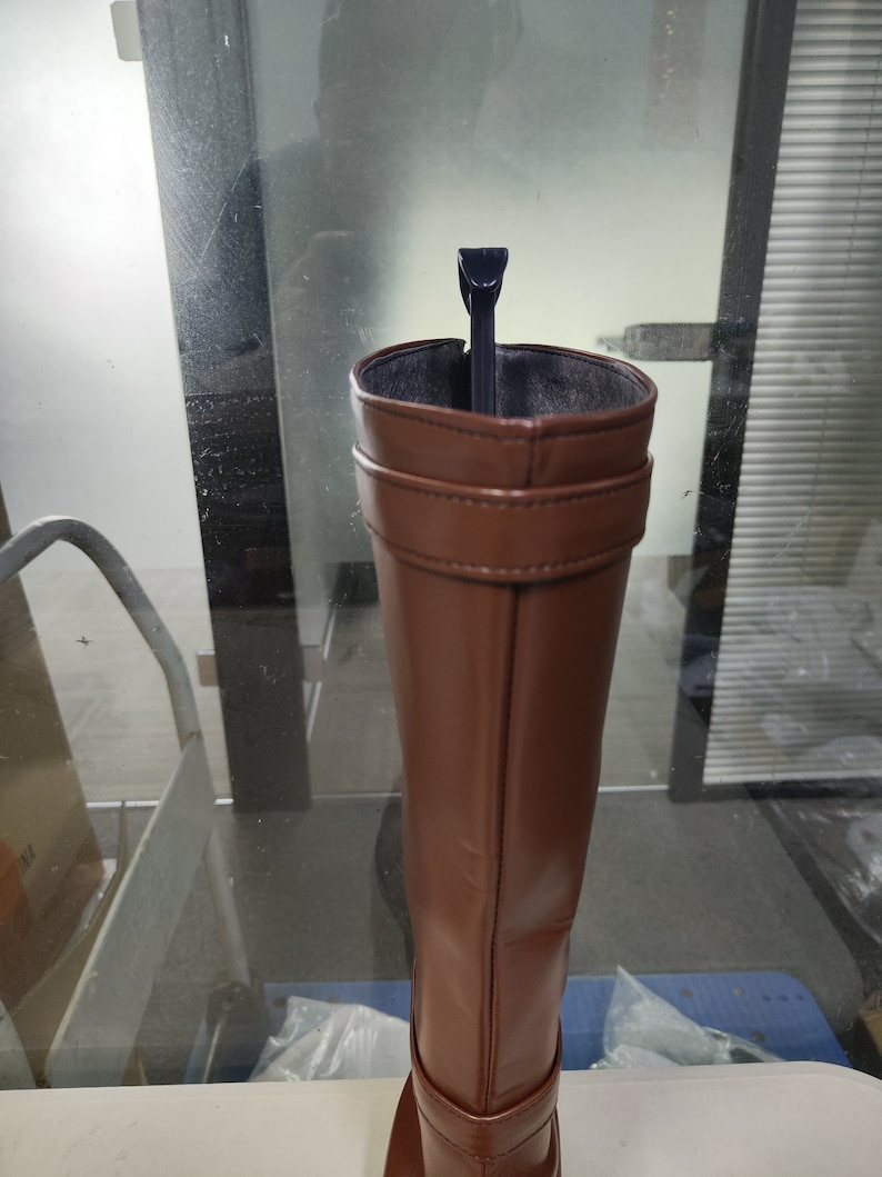 May include: A brown leather knee-high boot with a black boot stretcher inside.