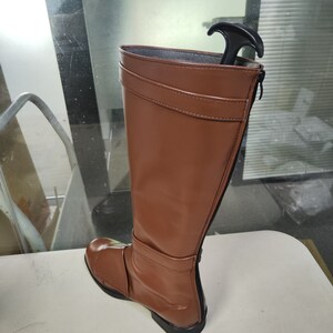 May include: A brown leather knee-high boot with a zip on the side and a black pull tab at the top.