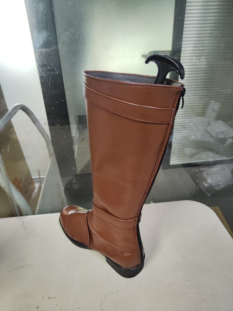 May include: A brown leather knee-high boot with a zip on the side and a black pull tab at the top.