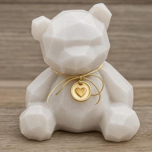 Könnte beinhalten: Weißes, geometrisch geformtes Teddybär-Figur mit goldenem Herzanhänger. Der Bär hat eine strukturierte Oberfläche und ein goldenes Band um den Hals. Er steht auf einer Holzoberfläche.