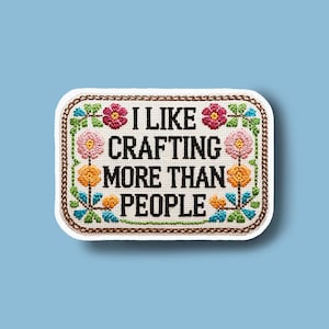 May include: Embroidered patch with the text "I LIKE CRAFTING MORE THAN PEOPLE" in black. The patch has a white background with a floral border in pink, orange, green, and blue. The border is brown.