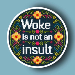May include: A round, black and white embroidered sticker with a colorful floral border. The text "Woke is not an insult" is written in white on a black background.