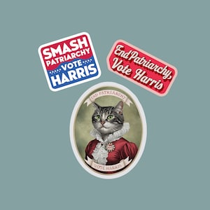 May include: Three stickers with a political theme. The first sticker is red, white, and blue and says "Smash Patriarchy Vote Harris". The second sticker is red and says "End Patriarchy Vote Harris". The third sticker is a round sticker with a cat wearing a red dress and a "Vote Harris" ribbon. The cat is wearing a "Vote" button.