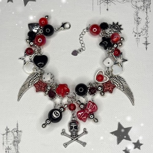 May include: A beaded bracelet with a gothic theme. The bracelet features red, black, and white beads, along with charms such as stars, hearts, dice, wings, an eight ball, a bow, and a skull with crossbones. The bracelet is silver in color.