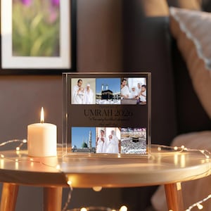 May include: A clear acrylic photo block with six images of Umrah 2026. The block has the text "Memories of Umrah 2026" and a lit candle on a wooden table. Decorative lights are wrapped around the table.