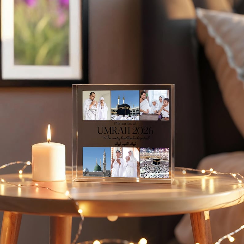 May include: A clear acrylic photo block with six images of Umrah 2026. The block has the text "Memories of Umrah 2026" and a lit candle on a wooden table. Decorative lights are wrapped around the table.