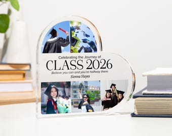 May include: A heart-shaped clear acrylic plaque featuring five printed photographs of graduates in caps and gowns. The text reads: Celebrating the Journey of CLASS 2026, Believe you can and you're halfway there, and the name Sienna Hayes.