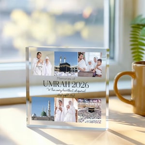 May include: A clear acrylic photo block featuring multiple images and the text "Memories of Umrah 2026." The block displays photographs of religious sites and people in white garments. The text includes English and Arabic phrases.