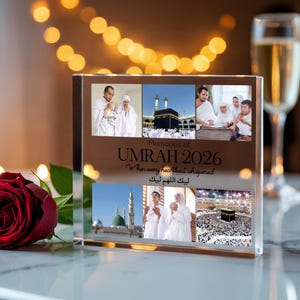 May include: A clear acrylic photo block with multiple images of religious sites and people. The block has the text "Memories of Umrah 2026" and other text in English and Arabic. A red rose and a glass of champagne are in the background.