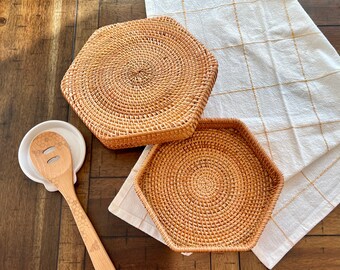 May include: A wooden honey dipper and spoon rest set with two woven rattan trivets and a white and gold checkered kitchen towel. The spoon has a honeycomb design and bee graphic. The trivets are hexagonal and square.