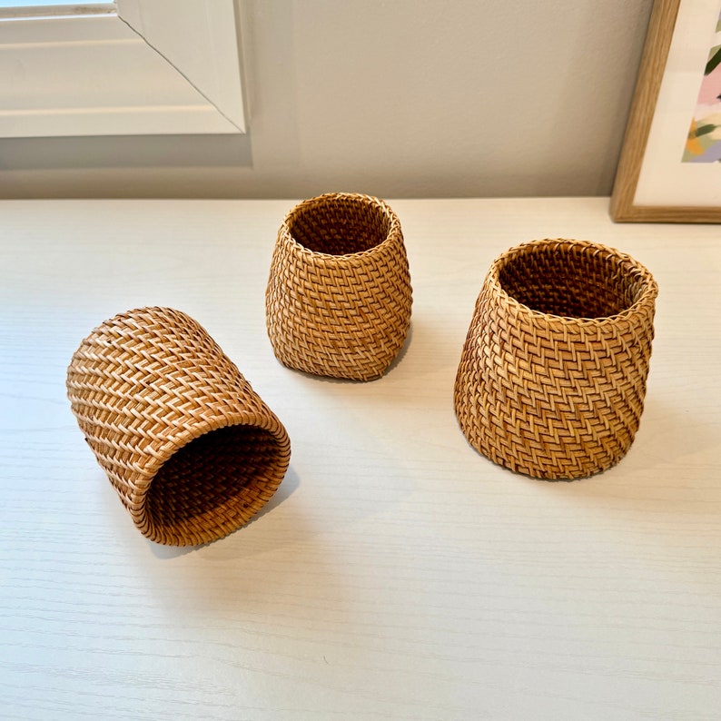 Pu&ograve; includere: Tre cestini in rattan intrecciato marrone chiaro. I cestini sono cilindrici con la parte superiore leggermente svasata. Il motivo intrecciato &egrave; visibile. Sono vuoti e disposti su una superficie bianca. Ogni cestino &egrave; alto circa 10 cm.