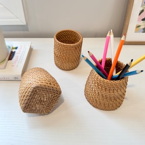 Pu&ograve; includere: Tre organizzatori da scrivania in rattan intrecciato. Un portapenne cilindrico contiene diverse matite colorate. Un secondo portapenne cilindrico &egrave; vuoto. Un terzo portapenne rettangolare pi&ugrave; piccolo &egrave; sdraiato su un lato.