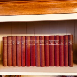 May include: A set of vintage "Railway Observer" books with red covers, spanning from 1967 to 1981. The spines are labelled with the title and year. The books are displayed on a white shelf, with a wooden shelf above.