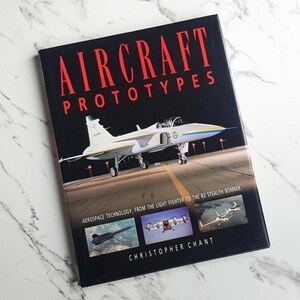 May include: A hardback book titled Aircraft Prototypes by Christopher Chant. The black cover features a large white fighter jet on a runway, with smaller images of aircraft below and the subtitle Aerospace Technology, From the Light Fighter to the B2 Stealth Bomber.
