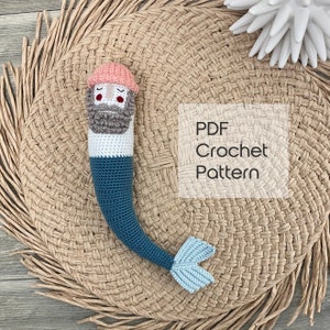 May include: A crochet pattern for a mermaid amigurumi toy. The toy is wearing a pink hat and has a gray beard. The pattern is available as a PDF download.