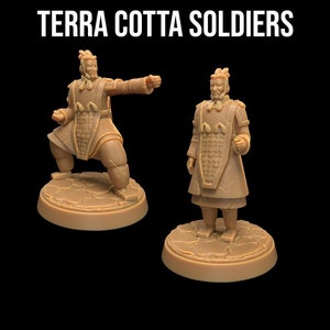 May include: Two terracotta soldier figurines, one standing and one in a fighting pose. Both are painted in a brown color and have detailed armor and facial features. The figurines are on circular bases.