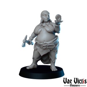Può includere: Una statuetta in miniatura dipinta di grigio di una donna che tiene un piccone e un oggetto rotondo. Indossa una gonna e una cintura. La statuetta è in piedi su una base nera.