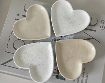 Puede incluir: Cuatro platos de cerámica en forma de corazón en varios tonos de blanco y beige. Los platos tienen un acabado moteado y están dispuestos en forma de trébol.