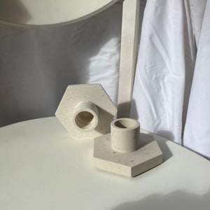 Può includere: Due portacandele esagonali bianchi con una finitura macchiettata. I portacandele hanno un'apertura rotonda al centro per una candela.