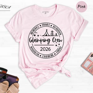 a pink t-shirt with a graphic design, a pair of sunglasses, a wallet, and a hat, all laid out on a white background.