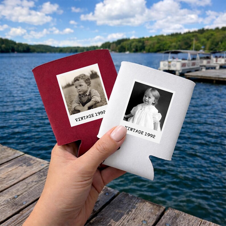 A hand holding two photo sleeves with black and white photos of children, with a body of water and a dock in the background.