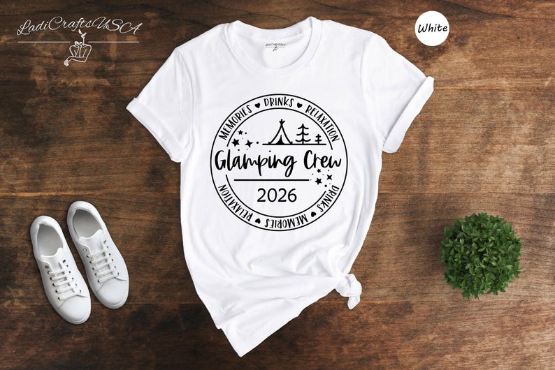 A white t-shirt with a graphic design, a pair of white sneakers, and a small green plant on a wooden surface.