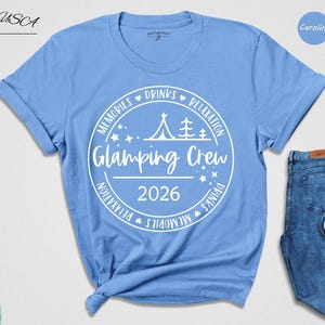 A blue t-shirt with a white graphic design, a pair of blue jeans, and a pair of blue sneakers, along with a hat and a green bag, all laid out on a white background.