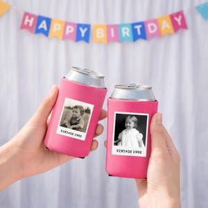 Two hands holding pink beverage holders with black and white photographs of children, against a background with a "Happy Birthday" banner.