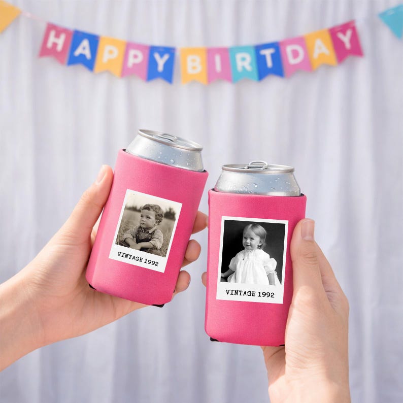 Two hands holding pink beverage holders with black and white photographs of children, against a background with a "Happy Birthday" banner.