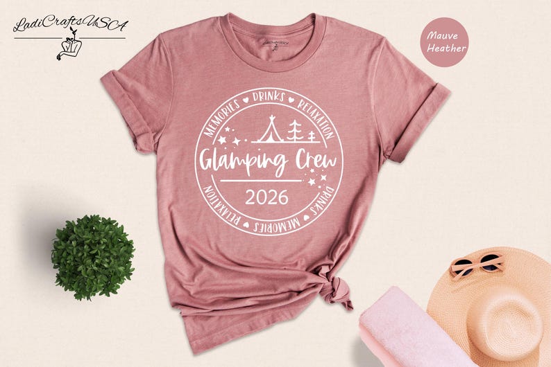 a pink t-shirt with a white graphic design, a small green plant, a hat, sunglasses, and a towel, all arranged on a light-colored background.