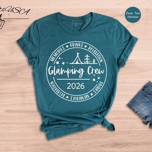 A teal t-shirt with a white graphic design, a pair of denim shorts, and a hat are displayed on a wooden surface.