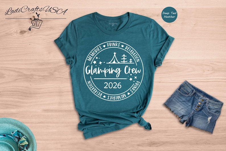 A teal t-shirt with a white graphic design, a pair of denim shorts, and a hat are displayed on a wooden surface.