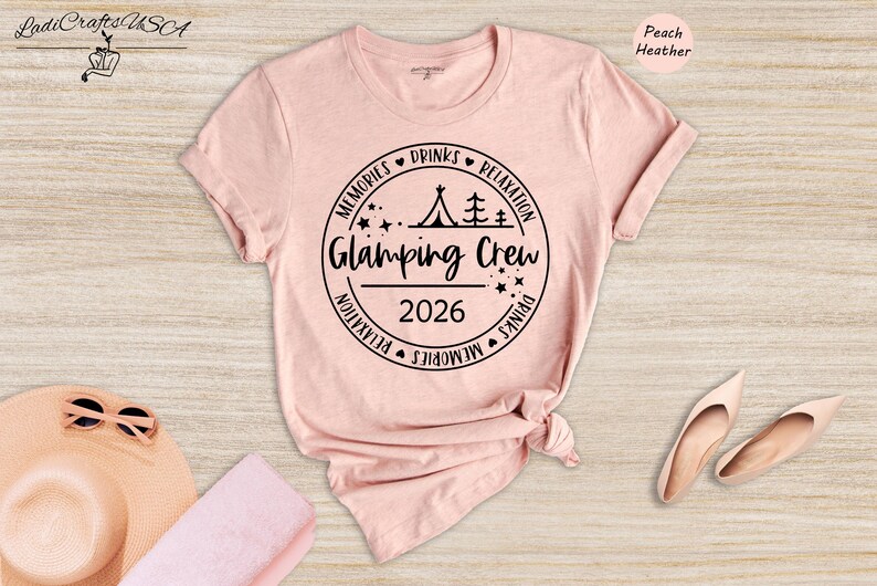 a pink t-shirt with a graphic design, a pair of sunglasses, and a hat, all placed on a wooden surface.