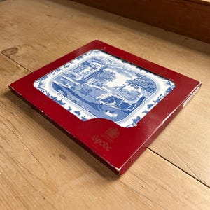 May include: A blue and white Spode decorative tray with a landscape scene, set in a red cardboard box. The tray features a detailed illustration of a classical landscape with figures and buildings. The Spode logo is visible on the box.
