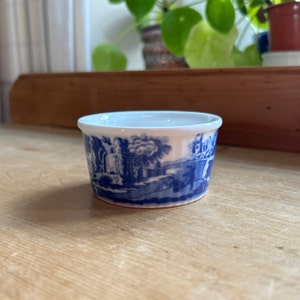 Puede incluir: Un pequeño ramequín de cerámica blanca con un patrón floral azul y blanco. El ramequín es perfecto para servir porciones individuales de postres o salsas.