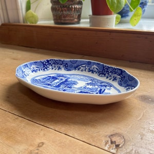 May include: A white oval serving dish with a blue and white floral pattern. The dish features a blue and white landscape scene with a building and trees.