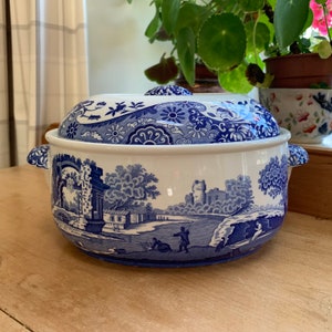 May include: A blue and white ceramic casserole dish with a lid. The dish features a traditional English country scene with a castle, trees, and figures. The lid has a floral pattern.