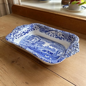 Puede incluir: Plato de servir rectangular de cerámica azul y blanca. El diseño central presenta una escena de paisaje detallada, rodeada de motivos florales y de volutas. El plato tiene un borde festoneado. El diseño recuerda a la porcelana clásica azul y blanca.