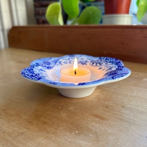 May include: A blue and white ceramic candle holder with a scalloped edge. A white tea light candle is burning inside the holder.