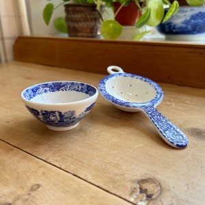May include: A blue and white porcelain tea strainer and a matching teacup. The strainer has a handle and a perforated bottom. The teacup is round and has a blue and white floral pattern.