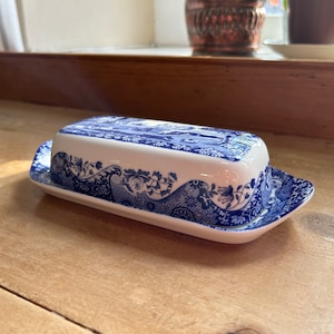 Op de afbeelding: Een blauwe en witte porseleinen botervloot met een bloemenpatroon. De vloot heeft een deksel en een basis.