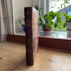 May include: A vintage, brown leather-bound book with gold accents and the title "Staunton's  Sports and Pastimes" on the spine.