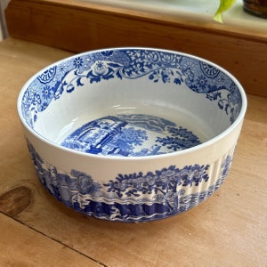 May include: A white ceramic bowl with a blue and white floral pattern. The bowl has a fluted edge and a scene of a blue and white landscape on the bottom.