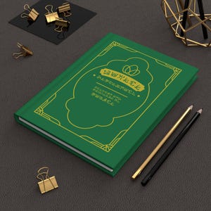 May include: A green journal with gold accents and text. The cover features a gold decorative border and a central design with text. Gold binder clips and pencils are also present.