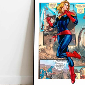 May include: A comic book page featuring Captain Marvel in a blue and red suit, with a red cape and red boots. She is standing on a destroyed building, with a red and yellow explosion behind her. The text on the page reads "A little pose of repulsor rays should motivate them to clear out." and "Our thanks, Avengers. That was a textbook display of combat tactics."