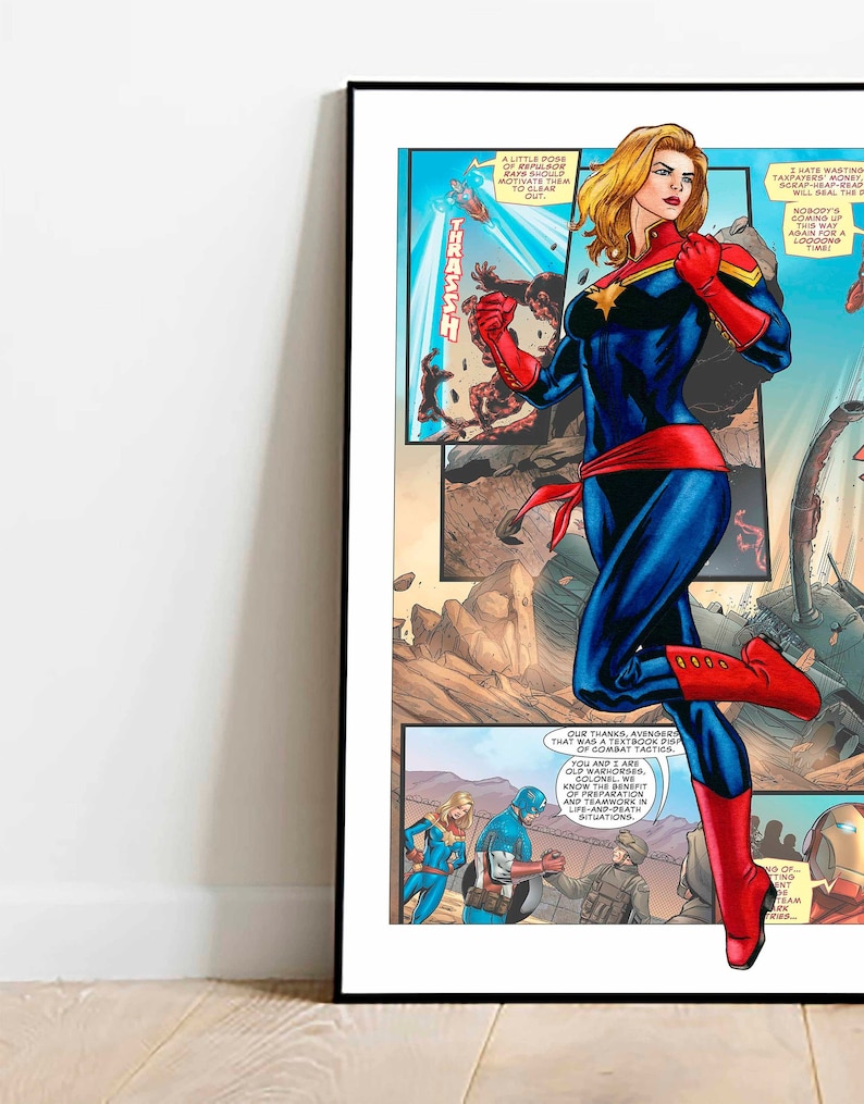 May include: A comic book page featuring Captain Marvel in a blue and red suit, with a red cape and red boots. She is standing on a destroyed building, with a red and yellow explosion behind her. The text on the page reads "A little pose of repulsor rays should motivate them to clear out." and "Our thanks, Avengers. That was a textbook display of combat tactics."